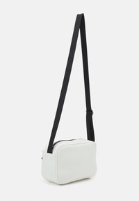 Biała syntetyczna torebka na ramię z czarnym regulowanym paskiem, prostokątnym kształtem, gładką fakturą i zamkiem błyskawicznym u góry.