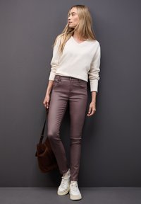 Suéter crema con cuello en V combinado con pantalones ajustados en tono vino. Tela texturizada y un bolso marrón de hombro. Zapatillas blancas completan el conjunto.