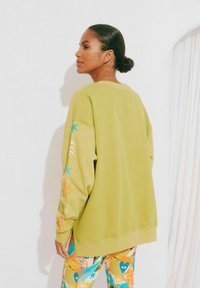 Groene sweatshirt met een oversized pasvorm, gestructureerde stof en kleurrijke patronen op de mouwen. Gepromoot met levendig gestreepte legging.