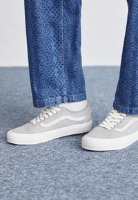 Baskets grises avec dessus texturé, accents blancs et semelles en caoutchouc, associées à un jean bleu à motifs.