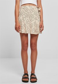 Jupe beige clair avec un motif floral noir, conception enveloppante, forme évasée et détail de nouage sur le côté. Le tissu semble lisse et léger.