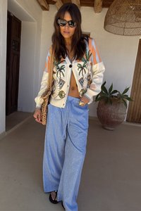 Knitted cardigan with palm tree embroidery in cream, orange striped details. Blue pinstriped wide-leg pants. Woven bag and black sandals.