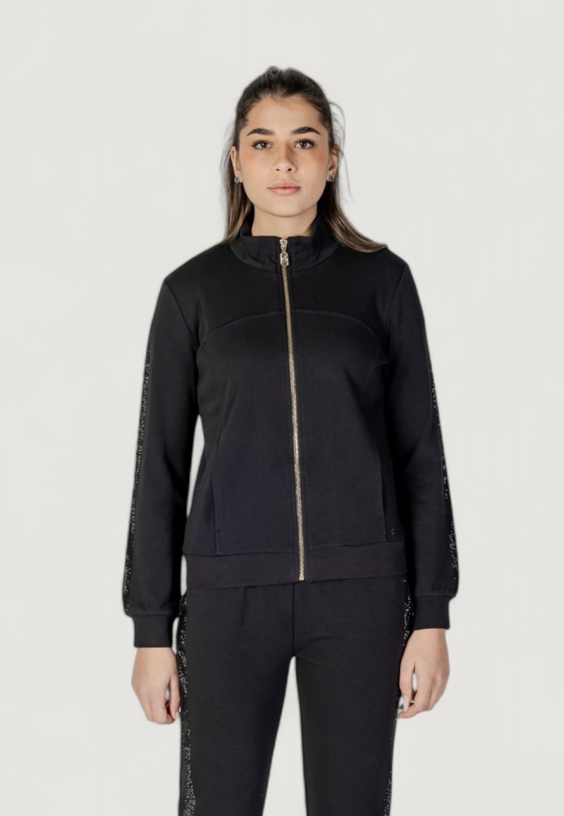 Giacca nera con zip e colletto alto, caratterizzata da maniche affusolate e dettagli testurizzati lungo il lato, realizzata in tessuto morbido.