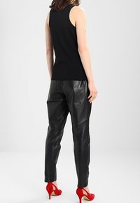 Haut sans manches noir associé à un pantalon en cuir noir. Modèle portant des escarpins rouges vif. Textures lisses et design ajusté.