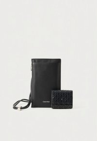 Mustast nahast rihmakott peene tekstuuriga rahakotiga. Kotil on sile viimistlus, õhuke siluett ja logo; rahakotil on geomeetriline muster.