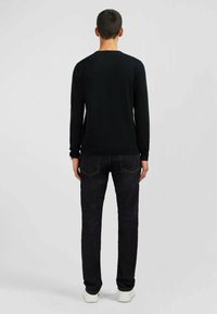 Chemise noire à manches longues avec un col rond, associée à un jean foncé et des baskets blanches. Design simple, silhouette ajustée, sans motif.