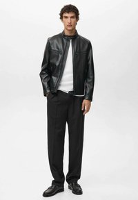 Black leather jacket with a high collar, two front pockets, and zip closure, paired with a white shirt, black trousers, and shoes.