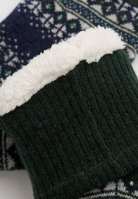 Vihreä neulottu neuletakin hiha, jossa on valkoinen fleece-vuori. Hiha on tummansinisellä taustalla, jossa on vihreitä ja norsunluunvärisiä geometrisia kuvioita.