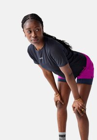 Black short-sleeve performance shirt with mesh texture, paired with vibrant pink and navy shorts. Accessories include gold bracelets and patterned socks.