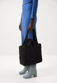 Czarna pikowana torebka na podwójnych uchwytach, z teksturowaną powierzchnią i poziomym wzorem przeszyć. W połączeniu z szarymi botkami na słupku.