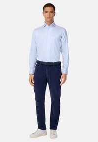 Gai zils svītrots krekls, apvienots ar tumši zila samta biksēm un baltām sporta kurpēm, ar teksturētu jostu un mūsdienīgu piegriezumu.