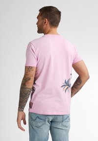 Camiseta rosa de manga corta con estampado de palmera en la parte posterior. Cuenta con un cuello redondo y está hecha de una suave tela de algodón.