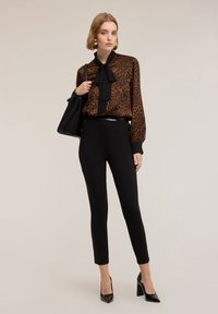Bluzka w brązowo-czarny wzór w cętki, z kołnierzykiem z kokardą, zestawiona z czarnymi, dopasowanymi spodniami i czarnymi lakierowanymi szpilkami. Dodatkiem torebka w kolorze czarnym.
