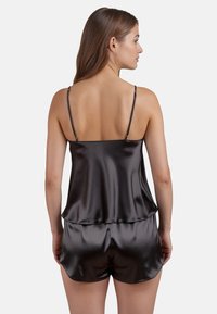 Set da notte in satin nero composto da un top con bretelline sottili e pantaloni corti ampi. Tessuto liscio con un design elegante e minimale.