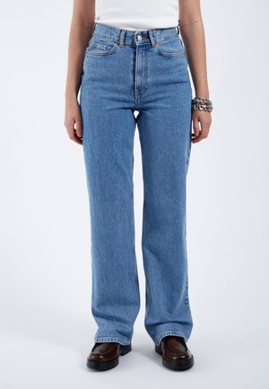 Light blue high-waisted jeans in a relaxed fit, featuring five pockets, button closure, and subtle fading. Worn with brown block-heel shoes.