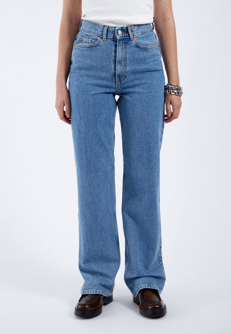 Ljusblå högmidjade jeans i avslappnad passform, med fem fickor, knäppning och subtila blekningar. Bärs tillsammans med bruna klackskor.