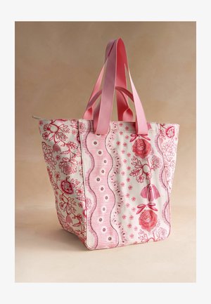 Raudonos ir baltos gėlėmis margintas rankinės krepšys su rausvų juostų rankenomis ir kutų detalėmis ant neutralaus fono.