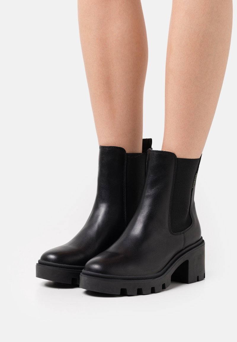 Stivali alla caviglia in pelle nera con pannelli elastici laterali, suole in gomma nera chunky e una finitura liscia. Progettati con una punta arrotondata.