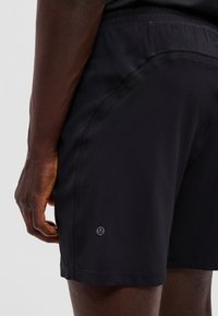 Mężczyzna w czarnych sportowych szortach Lululemon, pokazany z boku i z tyłu od talii do połowy uda z ręką swobodnie opuszczoną wzdłuż ciała.