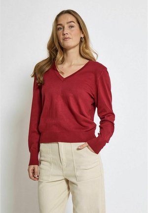Maglione rosso a scollo a V in morbido tessuto a maglia, con maniche lunghe e orlo a coste, abbinato a pantaloni beigi a vita alta.