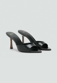 Mules noirs à bout ouvert avec une tige en cuir lisse, un bout carré et un talon haut élancé. Conçus avec des accents minimalistes.