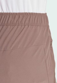 Lys brun elastisk midjebåndsmateriale med en strukturert overflate; sidelommelynlås for oppbevaring. Minimalistisk design, egnet for hverdagsbruk.