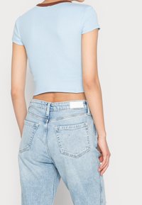 Světlomodré zkrácené tričko s hnědým žebrovaným výstřihem, kombinované se světlými denimovými džíny s klasickým pěti kapsovým designem.