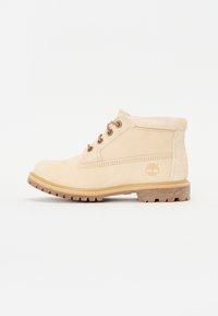Beige leren enkelboot met een suede kraag, ronde neus, bruine veters en een dikke rubberen zool. Heeft een geperst logo aan de zijkant.