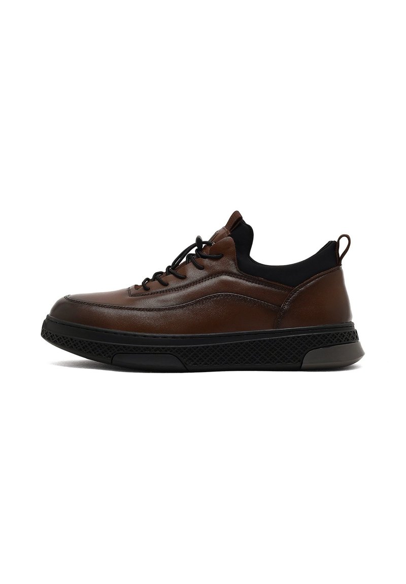 Sneaker en cuir brun avec semelle en caoutchouc noire, textures contrastantes, bout rond, fermeture à lacets et languette à l'arrière pour un enfilage facile.