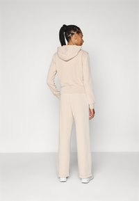 Beige, åtsittande huvtröja med dragsko och ribbade ärmslut, parat med vida byxor. Mjukt tyg med en slät textur och minimalistisk design.