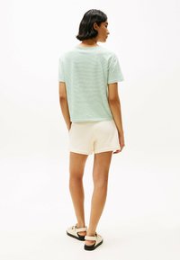 Camiseta de manga corta a rayas verdes y blancas, combinada con pantalones cortos crema. Sandalias negras con un detalle de tira. Atuendo simple y casual.
