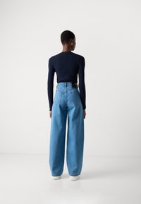 Navy blaues, geripptes Langarmshirt, kombiniert mit hochgeschnittenen, hellblauen Weitbeinen und weißen Sneakern; von hinten präsentiert.