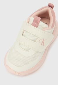 Dětská teniska krémové a růžové barvy s horní částí z síťoviny, zapínáním na suchý zip a logem "cK" na pásku.