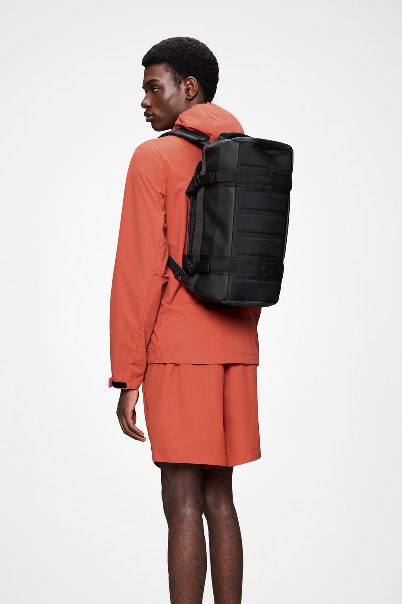 Zaino nero con spallacci regolabili, forma rettangolare, pannelli testurizzati e più punti di attacco, indossato sopra un completo rosso.