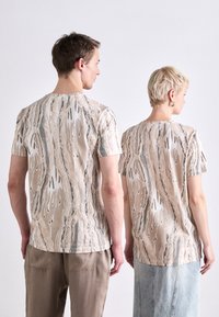 Kortermede t-skjorter i beige med et teksturert abstrakt mønster i krem, grå og rustfarger. Enkel design med rund hals.