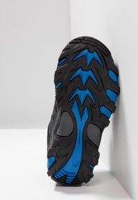 Schwarze Sportschuhsohle mit ausgeprägten blauen Akzenten. Die Sohle weist tiefe Rillen und eine strukturierte Oberfläche für besseren Halt auf.