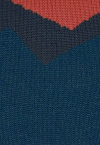 Dettaglio di un tessuto lavorato a maglia con motivo a zig-zag in colori rosso, grigio scuro e blu marina.