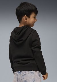 Felpa nera con una texture morbida e tasca a kangaroo, indossata da un bambino con capelli corti, abbinata a jeans di denim chiaro.