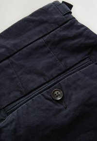 Pantalones de algodón azul marino con cierre de botón, bolsillos laterales y costuras decorativas en la cinturilla, con una textura suave.