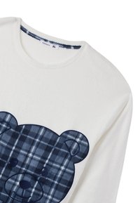 Biała bluza z nadrukiem pluszowego, granatowego misia w kratę, okrągłym dekoltem i miękką teksturą. Widoczna metka w rozmiarze XL.