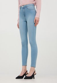 Chude dżinsy w jasnym niebieskim deninie z wysokim stanem, z przednią kieszenią i subtelnym przeszyciem. Połączone z czarnymi butami na słupku.