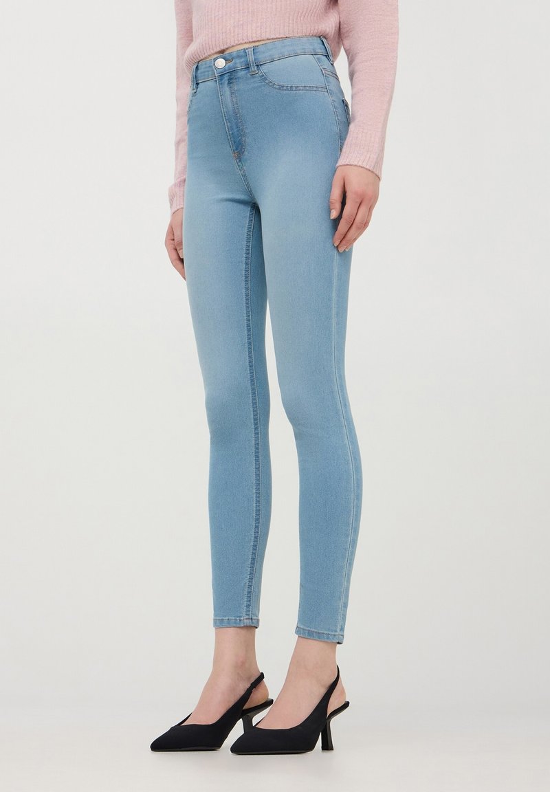 Chude dżinsy w jasnym niebieskim deninie z wysokim stanem, z przednią kieszenią i subtelnym przeszyciem. Połączone z czarnymi butami na słupku.
