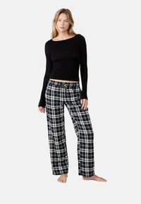 Top negro de manga larga con escote redondeado, combinado con pantalones de pijama de cuadros en blanco y negro, con cintura elástica y cordón.