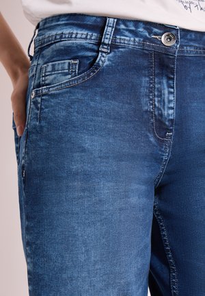 Nahaufnahme blauer Jeans an den Hüften einer Person, mit der Hand in der Gesäßtasche, sichtbare Knopfleiste und Nähte.