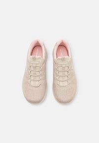 Baskets beiges avec une tige en maille texturée, des lacets élastiques et des semelles intérieures en mousse rose. Présence d'un logo sur le côté et d'un col rembourré.