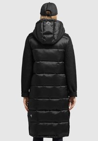 Czarna kamizelka puchowa z kapturem, o gładkiej powierzchni, grubych pikowanych segmentach i teksturowanych czarnych dzianinowych rękawach. Udekorowana logo z tyłu.