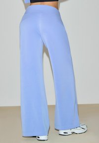 Ljusblå vida byxor med slät textur och hög midja, kombinerade med vita sneakers och en rak fåll. Enkel och stilren design.