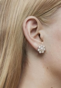 Pendientes en forma de flor de plata con acentos de perlas redondas. Textura brillante con múltiples elementos esféricos que rodean una perla central.