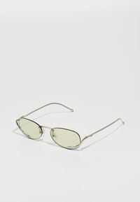 Ochelari de soare tip cat-eye cu ramă subțire din metal argintiu și lentile de culoare verde deschis. Prezintă un design elegant, hardware minim și ț temples curbați.