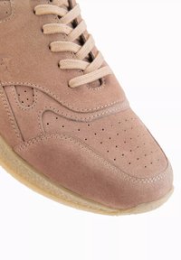 Ljusbruna mockaskor med perforerat tårum, krämfärgade snören och en strukturerad beige sula. Diskreta sömmar accentuerar designen.